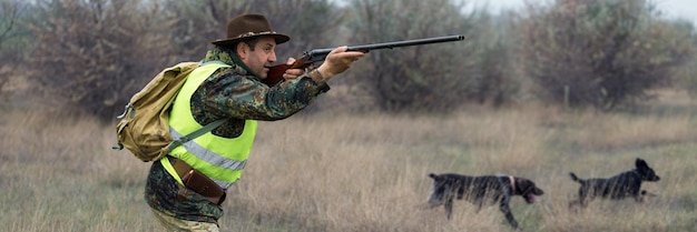 Hunting period autumn season open A hunter with a gun in his hands in hunting clothes in the autumn forest in search of a trophy A man stands with weapons and hunting dogs tracking down the game