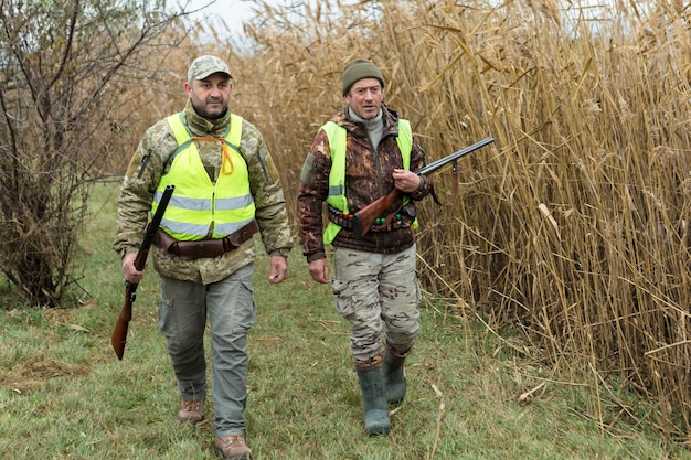 狩猟期間秋のシーズンが開くトロフィーを求めて秋の森で狩猟服を着て銃を手にしたハンター男が武器と狩猟犬を持って立ってgamex9xAを追跡している