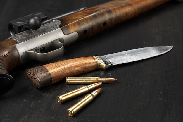 Hunting rifle and cartridges on dark wooden background