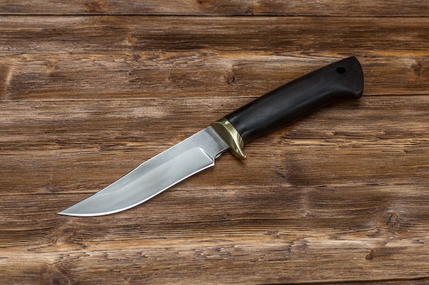 Coltello da caccia in acciaio fatto a mano su uno sfondo di legno marrone, primo piano