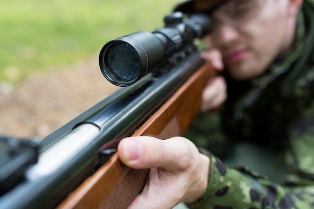 hunting, war, army and people concept - close up of young soldier, ranger or hunter with gun in forest