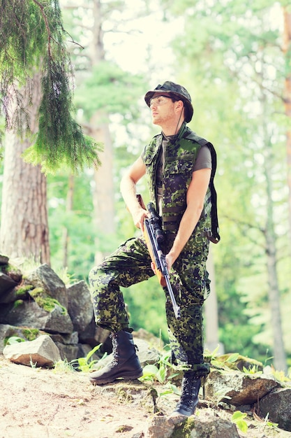 Foto concetto di caccia, guerra, esercito e persone - giovane soldato, ranger o cacciatore con pistola nella foresta