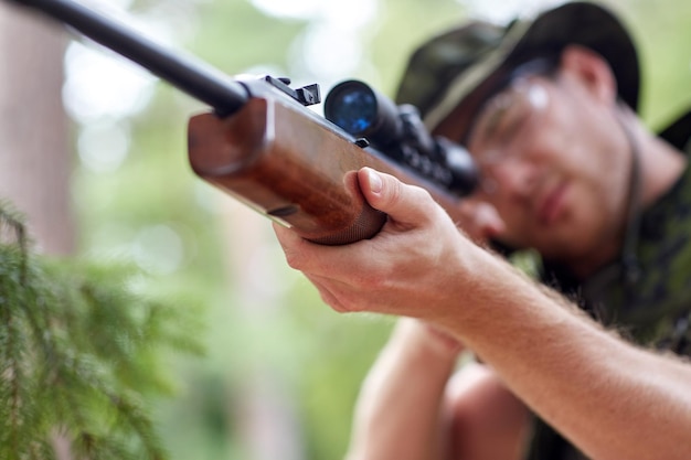 Photo hunting, war, army and people concept - young soldier, ranger or hunter with gun walking in forest