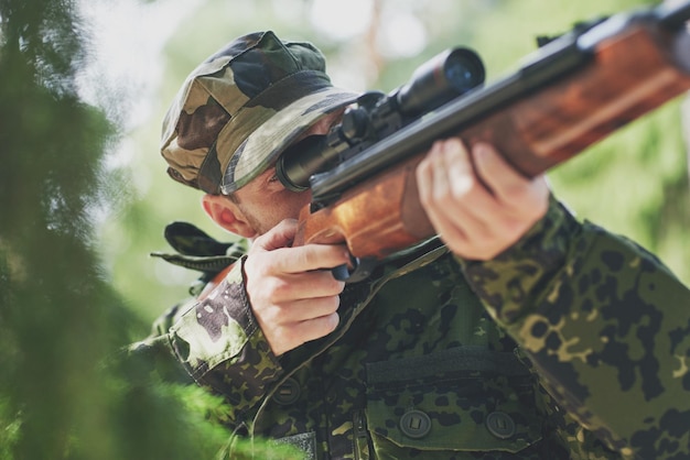 hunting, war, army and people concept - young soldier, ranger or hunter with gun walking in forest