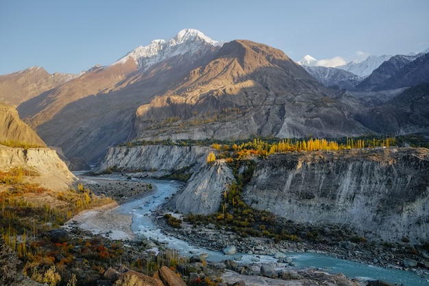 Hunza river flowing through Karakoram mountain range against clear blue sky in autumn. 
