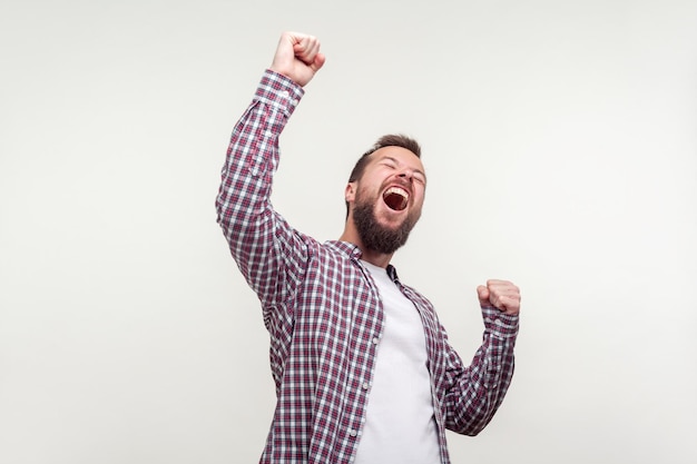 Hurray. Portrait of overjoyed winner, bearded man in casual plaid shirt raising hands, screaming yes i did it, emotionally reacting to success, victory. indoor studio shot isolated on white background