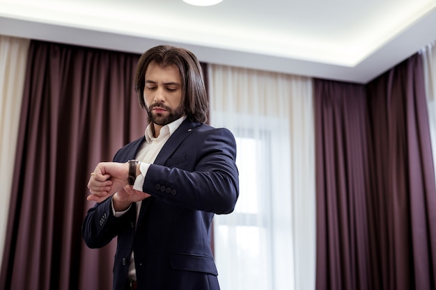 In a hurry. Handsome brunette man looking at his watch while checking the time