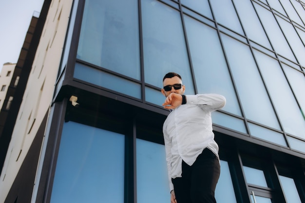 Hurry up for new day coming Waist up portrait of young attractive man looking on watch while talking by smartphone near window at home