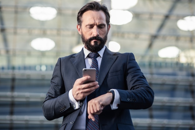 In a hurry. Waist up of a serious businessman checking time while holding a phone