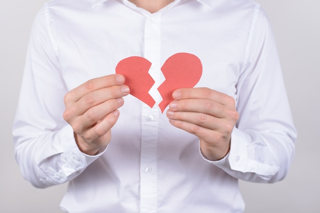 Hurt feelings marriage torn health care concept. Cropped close up photo of exhausted with bad feelings crying husband showing two halves on one heart isolated grey background