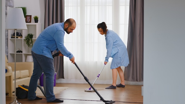 Фото Муж и жена вместе убирают дом с помощью пылесоса и швабры