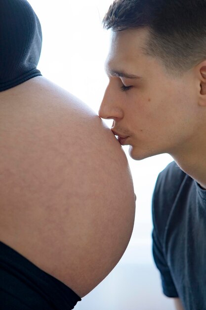사진 아기를 기대하는 남편과 아내 한 남자가 임신한 여성의 배에 키스를 하고 있다