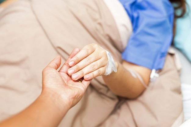 夫が病室で彼のアジア女性患者の手を握っています。