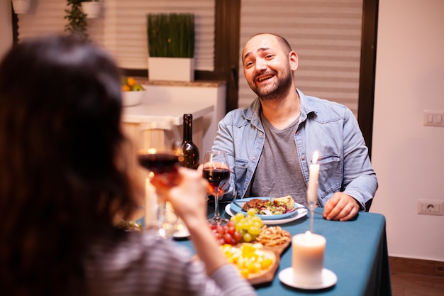Marito che sorride felice alla moglie durante una cena romantica. parlare felicemente seduti al tavolo della sala da pranzo, godersi il pasto a casa con momenti romantici a lume di candela.