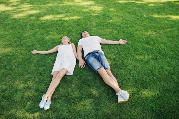 Husband and his pregnant wife lie on the grass. Top view. Relaxation outdoor