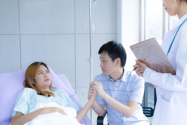 Husband holds the hand of a seriously ill wife with doctor at hospital