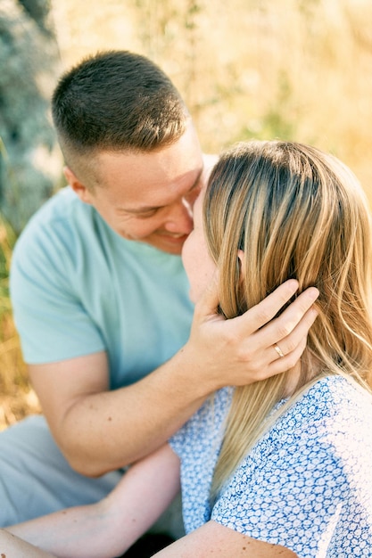 写真 夫は妻の顔を抱きしめて ⁇ 乾いた草の上に座ってほぼキスします ⁇