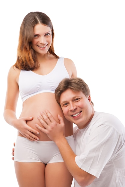 Husband listening to his wife&#39;s belly isolated over white