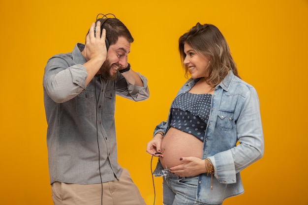 Husband plays listening to son beating his wife's belly using headphones. 