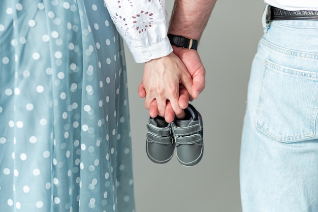 Husband and pregnant woman holding baby shoes in their hands closeup Motherhood family birth of a child