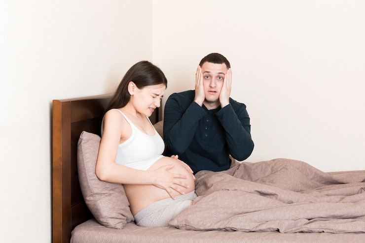 Photo 妊娠中の妻が家でベッドに横たわっている間 ⁇ 夫はショックを受けています ⁇ 