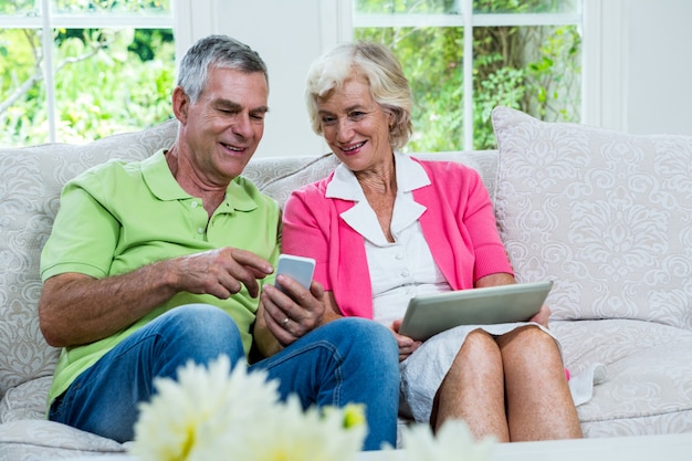 Husband showing mobile phone to senior woman on sofa