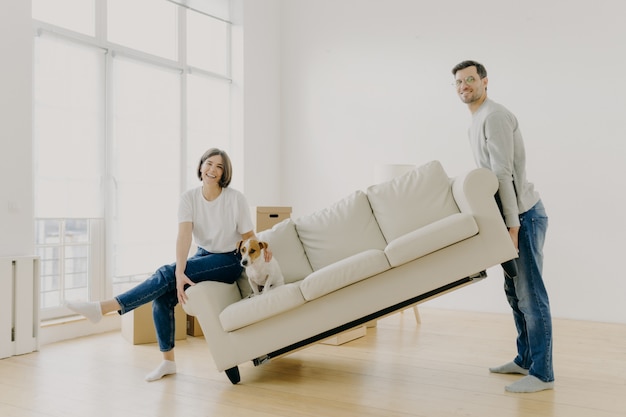 Husband and wife carry sofa, furnish living room after renovation, happy to buy apartment