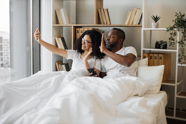 남편과 아내가 핸드폰으로 침대에서 자화상을 찍고 있다