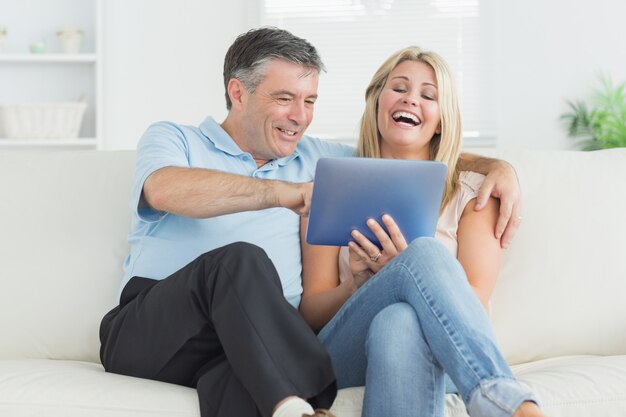 Husband and wife laughing at tablet pc on the sofa