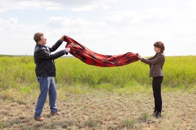 Husband and wife shaking dust and dirt off a blanket at a picnic.