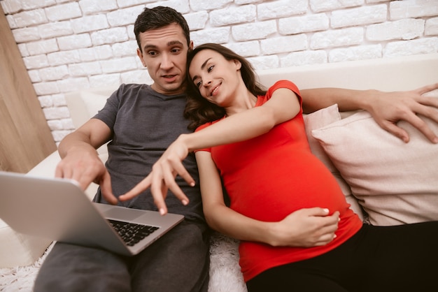 Husband and wife sitting together on sofa with laptop.