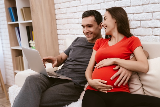 Husband and wife sitting together on sofa with laptop.