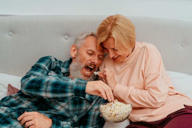 Husband and wife watch a film on the bed and eat popcorn