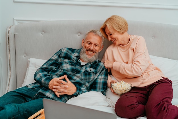 Husband and wife watch a film on the bed and eat popcorn