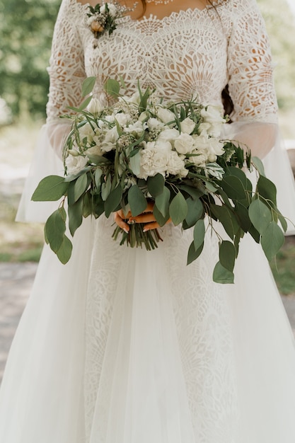 Huwelijksboeket met witte rozen en groene bladeren. bruid in jurk houdt boeket.