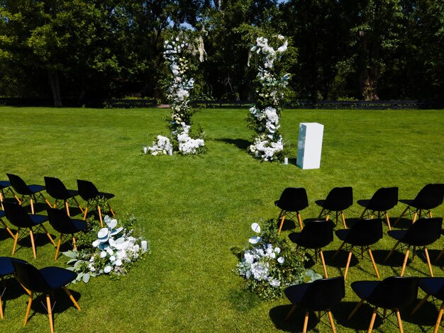 Huwelijksboog van witte bloemen en groene bladeren Zwarte gastenstoelen