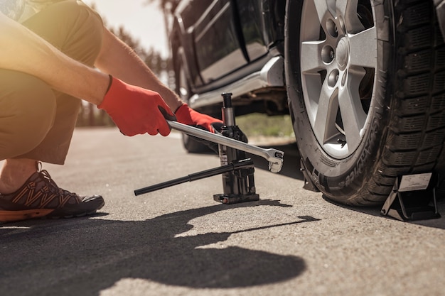 Hydraulic car jack is put under auto by hands in gloves closeup