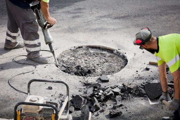 hydraulic hammer in the hands of an operator in uniform works the asphalt, partner collects rubble