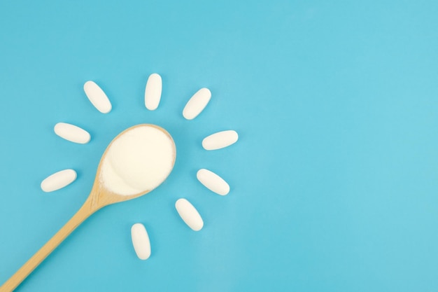 Hydrolyzed Marine Collagen Powder in wooden spoon and Vitamins in white tablets on blue background