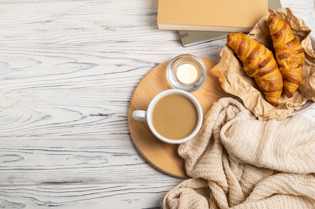 Hygge composition with coffee, candles, fresh croissants, notebook for writing and knitted plaid. Overhead flat lay