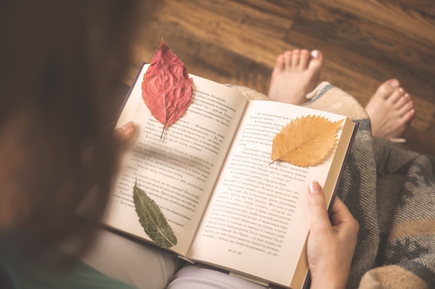 Foto concetto di hygge con ragazza e libro con foglie d'autunno. foto di sfondo accogliente a casa