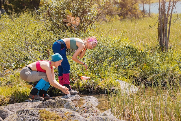 Foto hygiëne en verfrissing tijdens het wandelen in de wildernis twee meisjes wassen hun gezicht in een heldere stroom