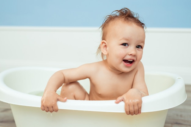 hygiëne en zorg voor jonge kinderen. een jaar oude baby baadt in de badkamer. Portret van een vrolijk lachend meisje dat in een klein bad met zeepachtig schuim baadt