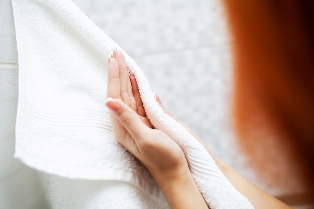 Hygiene and hand care. Woman using towel for wiping hands dry after washing in light bathroom at home.