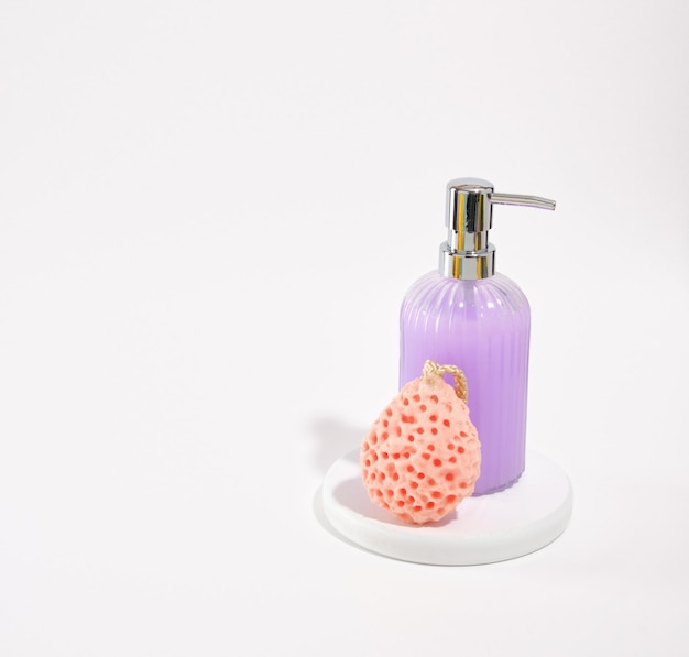衛生セルフケア製品紫色の液体石鹸ディスペンサーと白い背景に分離されたシャワー スポンジ テキスト用のスペースをコピーします。
