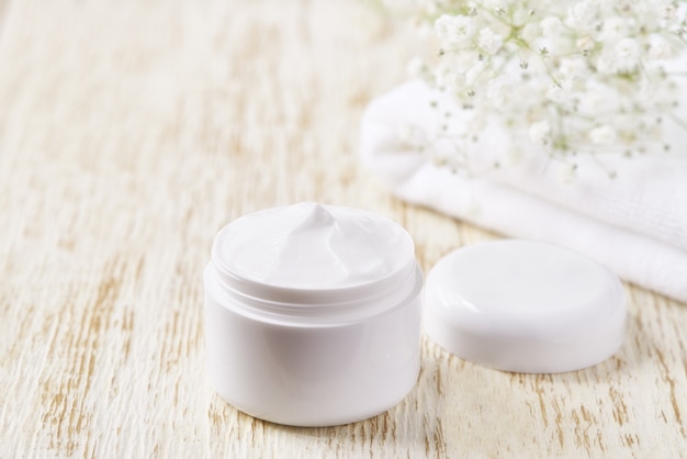 Hygienic cream skincare product  in plastic jar with towel on white table. Skin cleansing cosmetic cream or vitamin spa lotion, a natural organic herbal anti-wrinkle moisturizer.