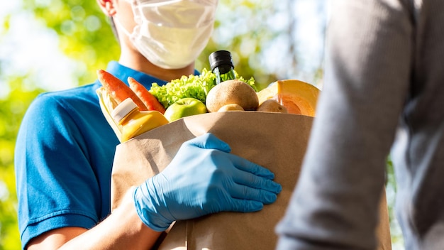 Fattorino igienico che indossa maschera facciale e guanti di gomma mentre consegna generi alimentari al cliente a casa, consegna di cibo al tempo del concetto di pandemia