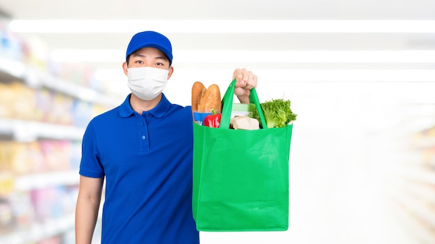 Hygienic man wearing medical mask holding grocery shopping bag in supermarket offering home delivery service