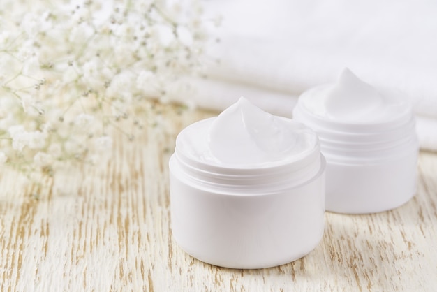 Hygiënisch crème huidverzorgingsproduct in plastic pot met handdoek op witte tafel. Huidreinigende cosmetische crème of vitamine spa-lotion, een natuurlijke biologische kruiden-anti-rimpel-moisturizer.