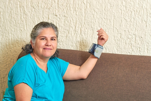 Hypertension concept and health care mature latina woman\
measures her blood pressure with digital monitor from home